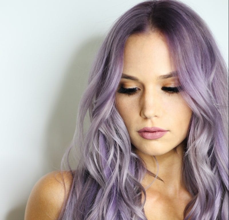 purple haired woman in black top leaning on wall